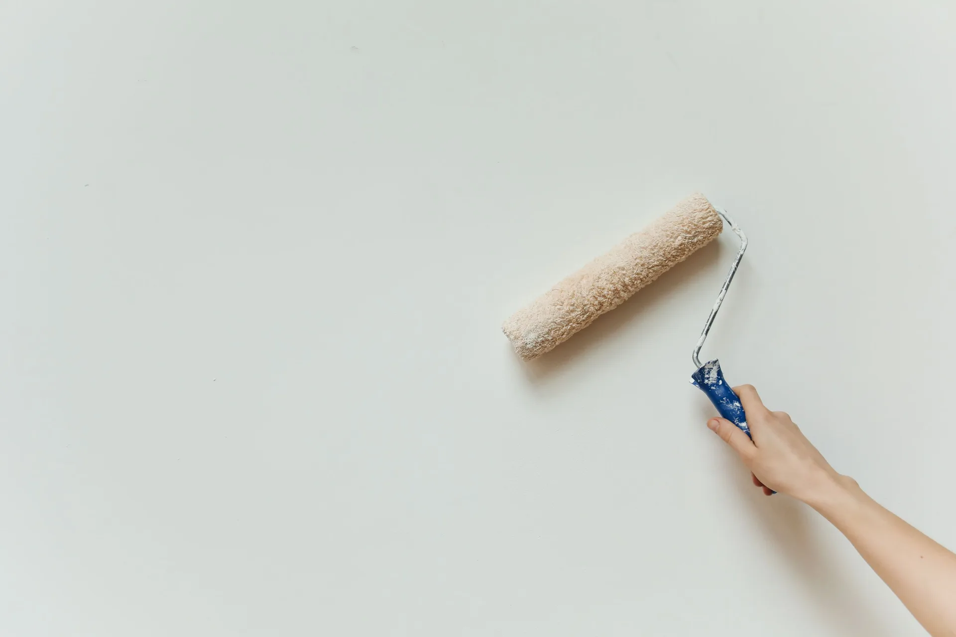 A hand holding a paint roller painting a wall